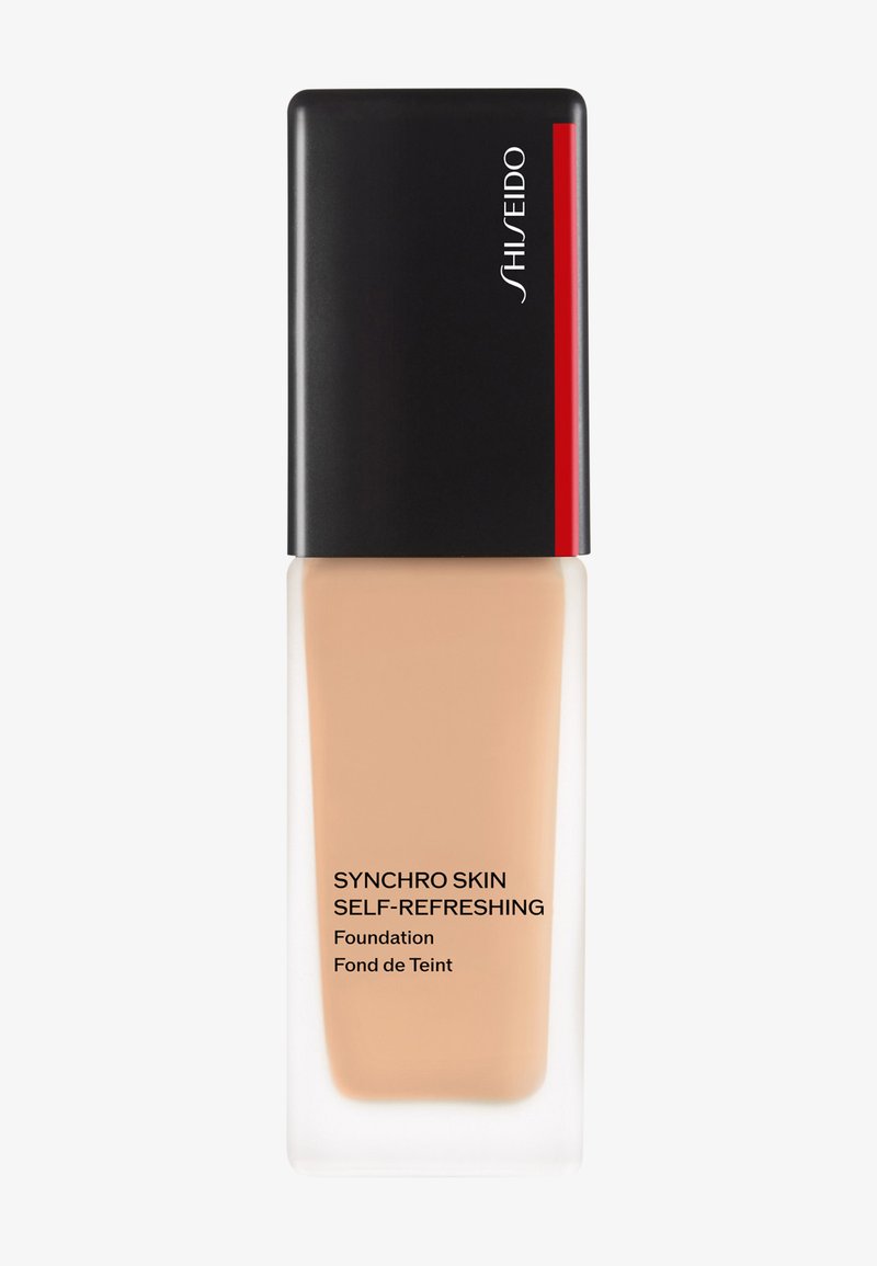 Podkład Shiseido Synchro Skin Self-Refreshing w przezroczystej szklanej butelce z czarną i czerwoną nakrętką; ciecz ma beżowy odcień.