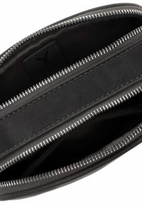 Interno di una borsa in pelle nera con chiusura a zip, caratterizzato da un materiale testurizzato e denti della zip metallici. Foderato in un tessuto scuro e liscio.