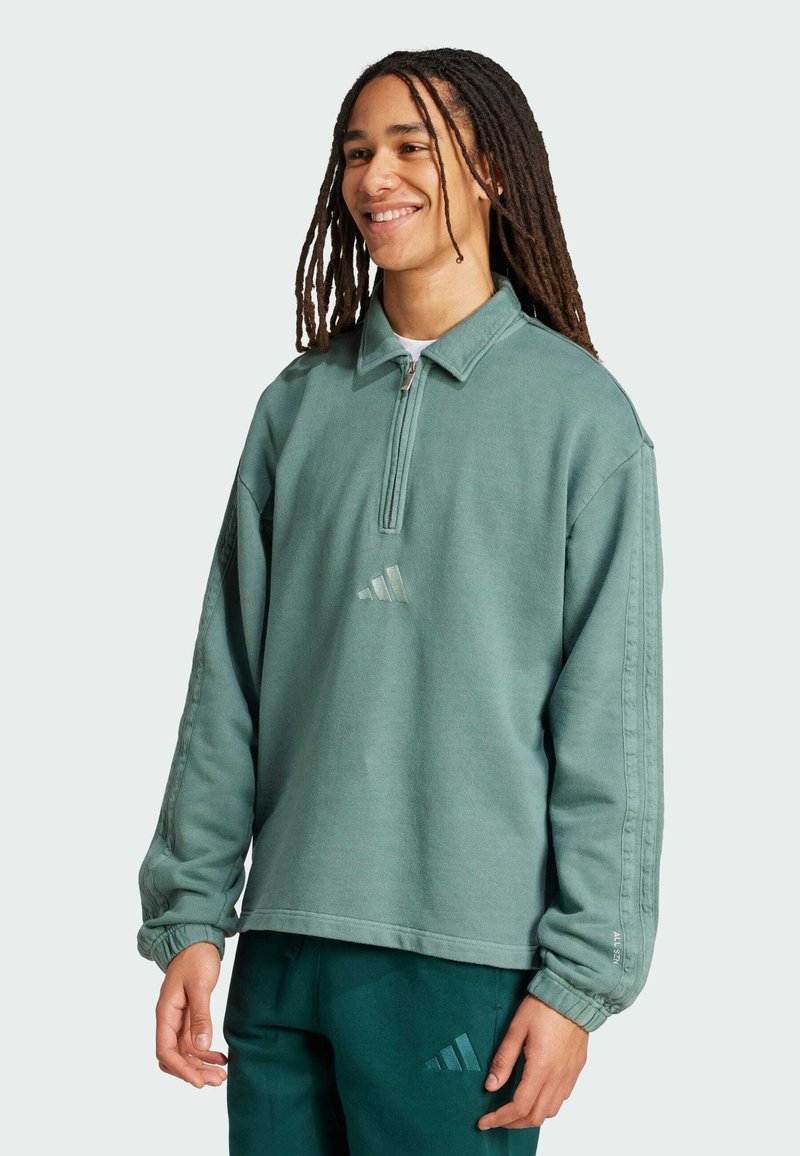 Ljusgrön sweatshirt med kvartsglipp, ribbad krage och långa ärmar. Har en adidas-logotyp i en något mörkare nyans.