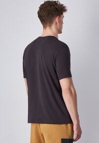 Camiseta de manga corta y cuello redondo en algodón gris oscuro, con una textura suave y un ajuste relajado, vista desde la parte trasera.