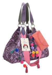 Grote paarse bloemen schoudertas van gestructureerde stof, met een roze strap, kleurrijke pompons en een koraal portefeuille die eraan bevestigd is. Inclusief een opvallend decoratief label.