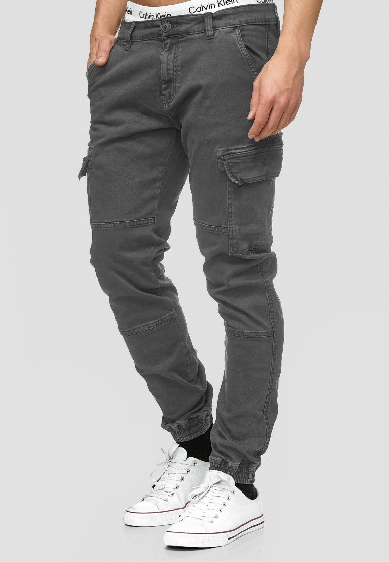 Pantaloni cargo grigi in cotone con multiple tasche, design affusolato e polsini elastici. Abbinati a sneakers bianche e con una vita visibile.