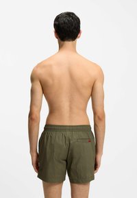 Gröna badshorts i lättviktigt material med elastisk midja och en bakficka med en liten röd etikett. Enkel design.