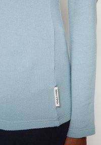 Ljusblå texturerad tröja med en sid sömsetikett. Materialet har ett vävt mönster och designen har en åtsittande form med långa ärmar.