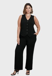 Svart skräddarsydd väst med V-hals och sex knappar, parat med vida svarta byxor. Minimalistisk design med sidfickor och stilrena klackar.