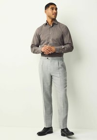 Brown patterned long-sleeve shirt with a collar, paired with light gray tailored trousers and black dress shoes.
