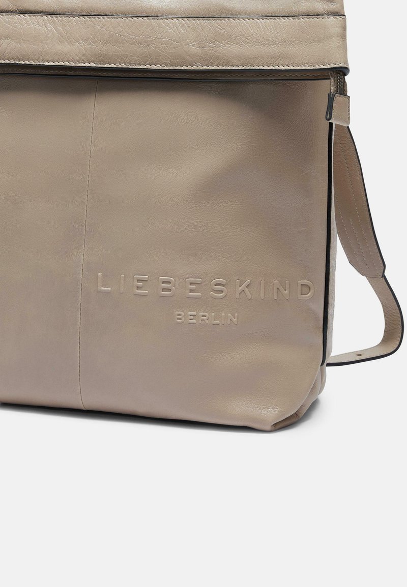 Beige Leder-Umhängetasche mit einer glatten Textur, verziert mit einem geprägten Logo, verstellbarem Trageriemen und einem minimalistischen Design.