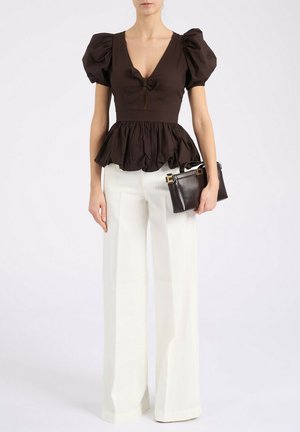 Mujer con blusa negra de mangas abullonadas y peplum, y pantalones blancos de pierna ancha, sosteniendo un pequeño bolso de cuero negro.