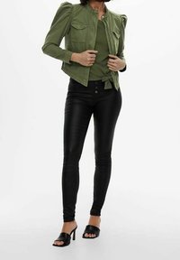 Grøn denimjakke med puffdetaljer på skuldrene, parret med en knyttet grøn top og sorte skinny jeans i faux læder. Åben tå sorte hæle sandaler.