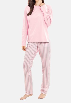 Donna con top rosa chiaro a maniche lunghe e pantaloni del pigiama rosa a righe, in piedi scalza contro uno sfondo semplice.