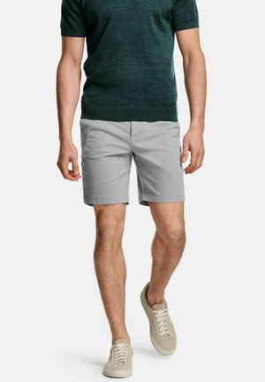 Shorts gris à texture lisse, associés à un pull à manches courtes vert foncé. Baskets kaki avec un design de lacets simple.