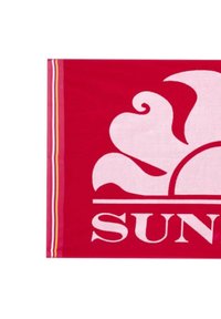 Asciugamano da spiaggia rosso con un grande motivo floreale bianco e la parola "SUN" in caratteri in grassetto. I bordi laterali presentano sottili strisce gialle e bianche.
