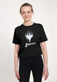 Černé bavlněné tričko s bílým designem, na kterém je stylizovaná ruka a slovo "Zendikar!" pod ní. Kulatý výstřih a krátké rukávy.