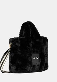 Borsa a mano in pelliccia sintetica nera con una texture morbida, caratterizzata da una forma rettangolare e una patch con logo. Include una tracolla a strisce e hardware dorato.