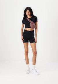 T-shirt noir raccourci et shorts taille haute, associés à un sac bandoulière rose clair et des baskets blanches avec des lacets texturés.