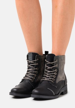 Schwarze Leder-Stiefeletten mit grauem Hahnentrittmuster an den Seiten, grauen Schnürsenkeln und strukturierten Gummisohlen. Mit Zuglasche an der Rückseite.