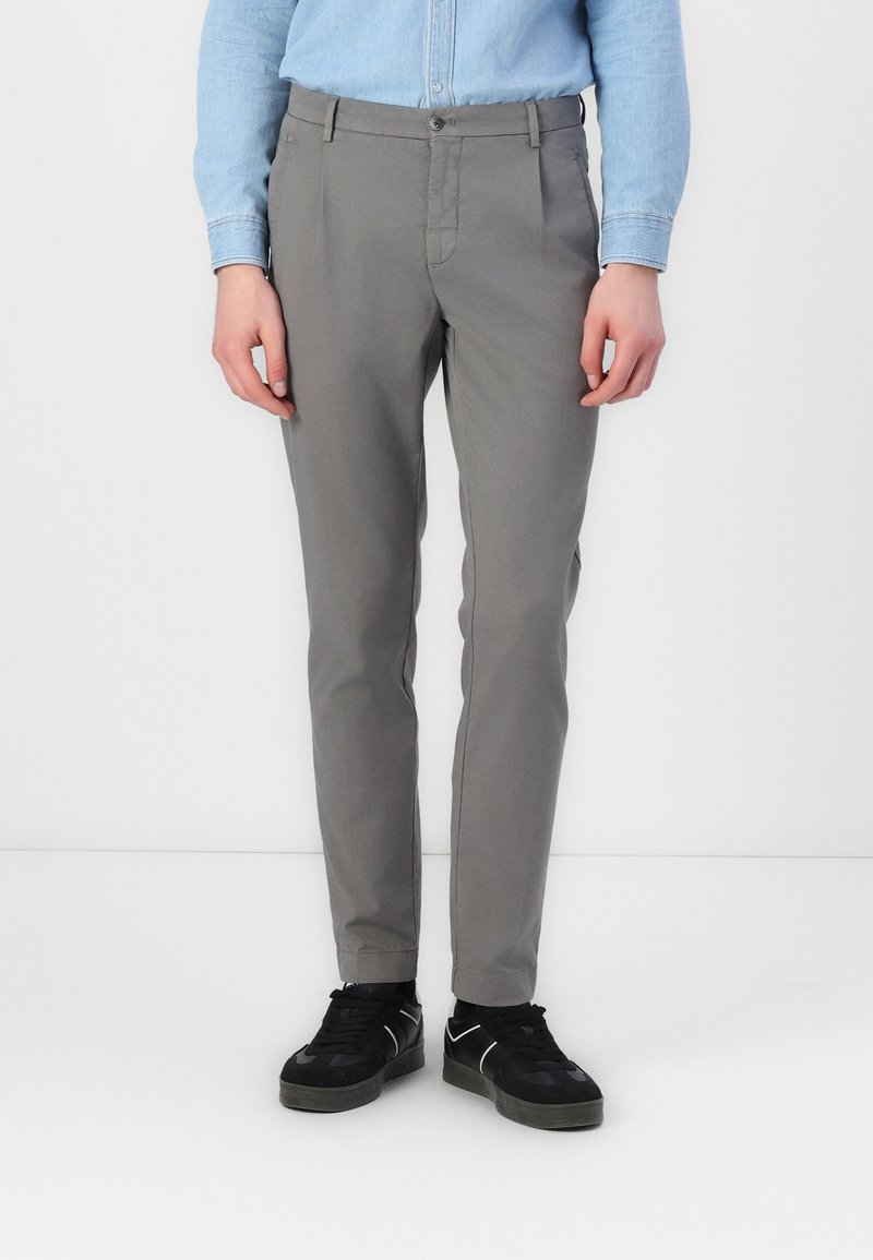 Pantalons slim gris clair à devant plat, avec poches latérales et passants de ceinture, associés à des baskets noires avec des accents blancs.