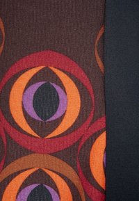 Tissu avec un motif géométrique comprenant des nuances d'orange, de violet et de marron, accompagné d'un tissu uni de couleur sombre. Les motifs incluent des cercles et des ovales.