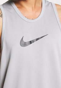 Canotta grigia in rete con scollatura arrotondata e accento del logo Nike in nero. Materiale leggero e traspirante con una finitura testurizzata.