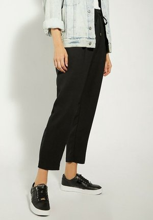Osoba ubrana w czarne krótkie spodnie, czarne sneakersy na platformie oraz jasną kurtkę dżinsową z podwiniętymi rękawami.