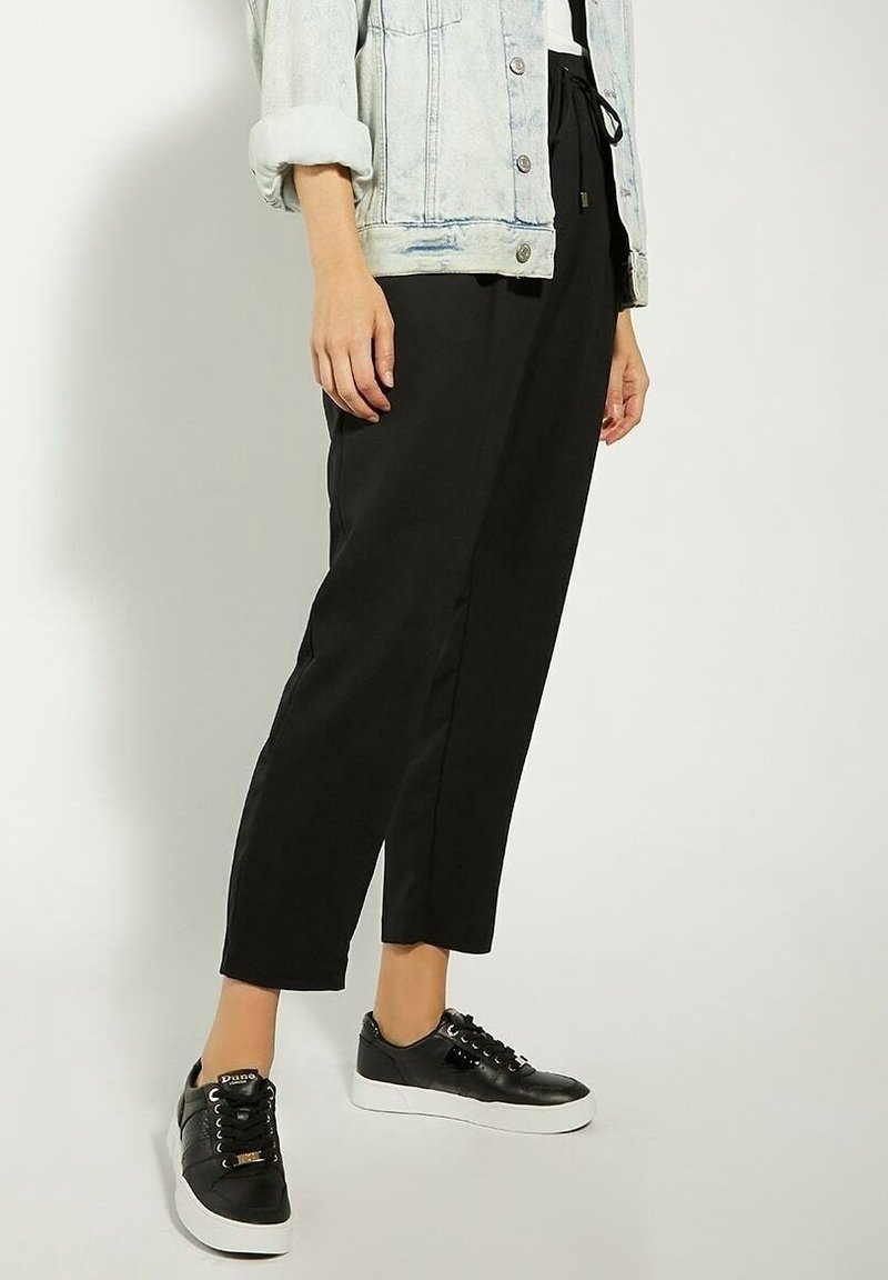 Personne portant un pantalon court noir, des baskets noires à plateforme et une veste en jean claire avec les manches retroussées.