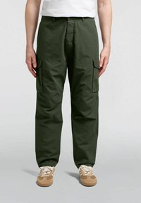 Pantaloni cargo in tessuto verde scuro con una vestibilità rilassata, dotati di due tasche laterali e cuciture rinforzate, abbinati a sneaker beige.