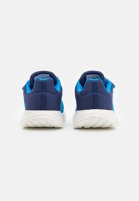 Chaussures de sport bleu marine et bleu avec une tige en tissu mesh, semelle blanche rembourrée et détails texturés au talon. Vue arrière.