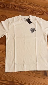 Camiseta blanca de Levi's sobre un suelo de madera con el logo "PLANTAS DE CASA" en negro en el lado izquierdo del pecho y etiqueta negra de Levi's adjunta.