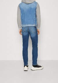 Jeansjacka med ljusblå tvätt, grå hoodieärmar och blå jeans. Svartvita sneakers fulländar outfiten.