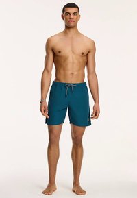 Türkiissinised ujumispüksid, valmistatud kerge kangaga. Sellel on elastne vöökoht nööriga ja väike logo küljes. Silmadele meeldiv ja siledapoolne tekstuur.