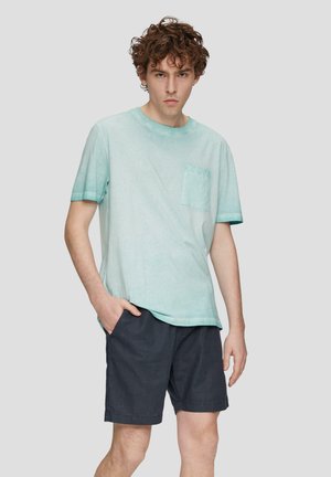 Helles blaues Baumwoll-T-Shirt mit einer Tasche, kurzen Ärmeln und einer lässigen Passform, kombiniert mit dunkelblauen Shorts.