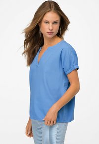 Top corto azzurro a maniche lunghe con scollatura a V e risvolti. Realizzato in tessuto leggero con una texture liscia. Abbinato a pantaloni a righe.