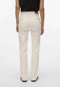 Jeans de pierna ancha beige con bolsillos traseros y una etiqueta marrón en la cintura. Fabricados con un suave material de algodón texturizado.