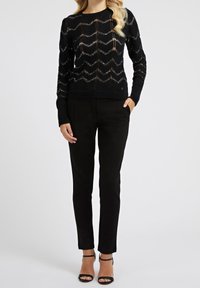 Maglione lavorato a maglia nero con motivo a zigzag, maniche lunghe e scollatura rotonda, abbinato a pantaloni neri aderenti e décolleté neri con cinturini.