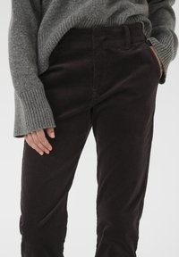 Mustat corduroypohkeet suoran istuvuuden kanssa, joissa on sileä rakenne, leveä vyötärönauha ja sivutaskut, yhdistettynä harmaaseen neulepaitaan.