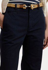 Námornícke chinos nohavice so slim fit strihom, s bočnými vreckami a lanovým opaskom v béžovej farbe s koženými akcentmi a kovovou sponou.