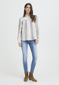 Blouse crème à rayures verticales bleues, col rond et fermeture à boutons, associée à un jean skinny bleu clair et des bottines marron.