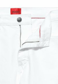 Weiße Jeansshorts mit einem roten Etikett mit "HUGO," einem silbernen Knopf und einem Reißverschluss mit sichtbaren Nähdetails.
