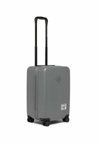 Valise rigide grise avec double poignée, deux roues et un logo en forme de diamant. Texture lisse et design simple.