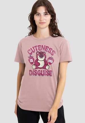 Young woman with long brown hair wearing a pink T-shirt featuring a pink bear and text "Cuteness is my disguise."
