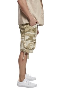 Kamouflage cargoshorts i beige och krämfärg, med flera fickor, dragsko vid benen och en lös passform, i kombination med vita sneakers.