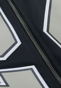 Schwarzer Stoffabschnitt mit einem silbernen Reißverschluss, der geometrische graue und weiße Muster aufweist. Die Naht ist sauber und das Material erscheint glatt.