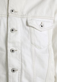 Vit denimjacka med metallknappar, bröstficka och dubbla sid sömmar med ljusa stygn. Slät textur, strukturerad passform.