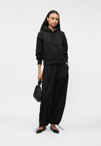 Μαύρη κουκούλα με τσέπη καγκουρό και κορδόνι, συνδυασμένη με μαύρο φαρδύ παντελόνι. Οι μαύρες μπαλαρίνες και μια μικρή μαύρη τσάντα ολοκληρώνουν την εμφάνιση.