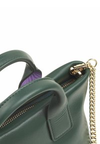 Sac en cuir vert avec une fermeture éclair dorée et une bandoulière en chaîne, présentant un intérieur texturé en violet. Deux poignées pour le transport.
