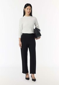 Maglione bianco lavorato a maglia con maniche lunghe, abbinato a pantaloni neri a gamba larga con una texture liscia e cuciture verticali. Gli accessori includono una borsa nera.
