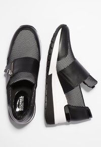 Sneaker in bianco e nero con tomaia in mesh, dettagli in pelle, cinturino regolabile e suola spessa bianca con battistrada testurizzato.