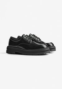 Scarpe in pelle nera con finitura lucida, design con lacci, colletto imbottito e suola in gomma testurizzata con motivi di tasselli.