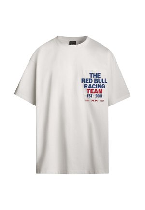Camiseta blanca de algodón con un bolsillo en el pecho que presenta texto en azul y rojo: "EL EQUIPO DE CARRERAS RED BULL EST. 2004" y un logo debajo del texto.