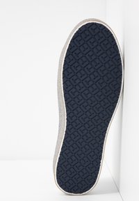Semelle d'une chaussure de sport avec une bande de roulement en caoutchouc noir présentant un motif de grille géométrique, affichée sur fond blanc.